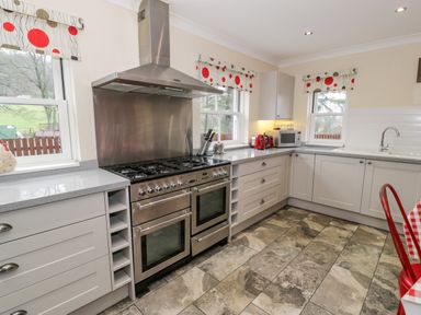 A kitchen with a stainless steel stove and hood a microwave kettle and toaster on the countertop and patterned window blinds at The Farm House in Bala