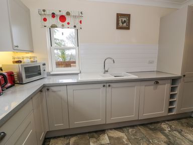 A kitchen with white cabinets a gray countertop a double sink a microwave and a window with a patterned blind at The Farm House in Bala