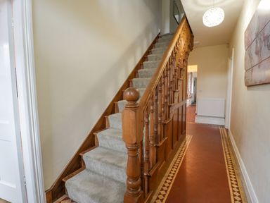 A hallway with a wooden staircase with carpet and patterned tile floor at The Farm House in Bala