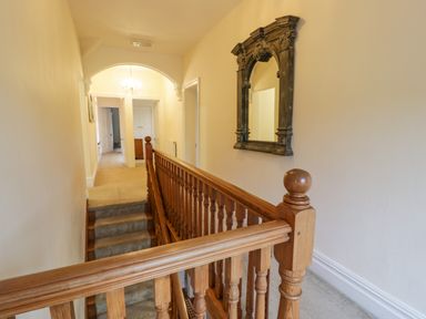 A hallway with wooden staircase railing and a decorative wall mirror at The Farm House in Bala