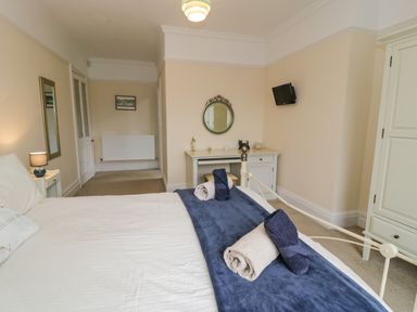 A bedroom with a bed covered in white linens and rolled towels on a blue runner at The Farm House in Bala