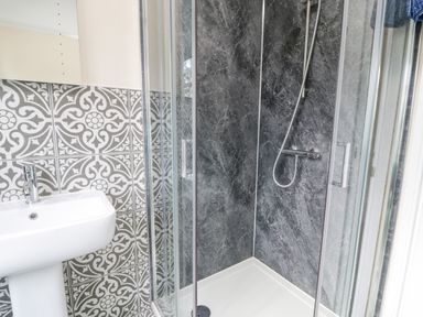 A bathroom with a shower enclosure and a sink with patterned tiles on the wall at The Farm House in Bala