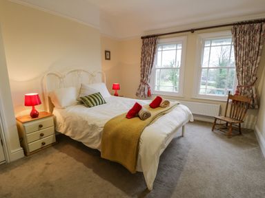A bedroom with a double bed two red lamps on bedside tables two windows and a wooden chair at The Farm House in Bala