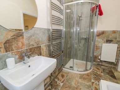 A bathroom with a sink a round mirror a shower enclosure and a radiator at The Farm House in Bala