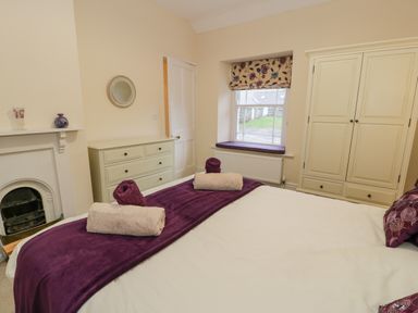 A bedroom with a bed with towels on a purple runner a dresser a wardrobe and a window at The Farm House in Bala