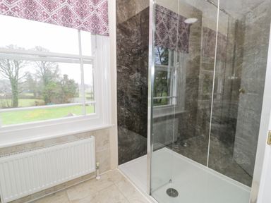 A bathroom with a glass shower enclosure a window with patterned blinds and a radiator below at The Farm House in Bala