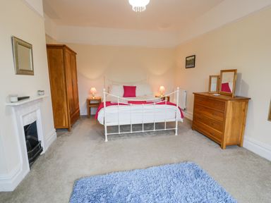 A bedroom with a white bed and pink bedding two wooden nightstands with lamps a wooden wardrobe a wooden dresser with mirrors a fireplace and a blue rug on the floor at The Farm House in Bala