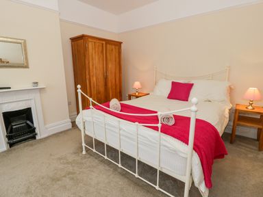 A bedroom with a white metal bed frame with pink cushions and blankets wooden wardrobe bedside tables with lamps and a fireplace at The Farm House in Bala