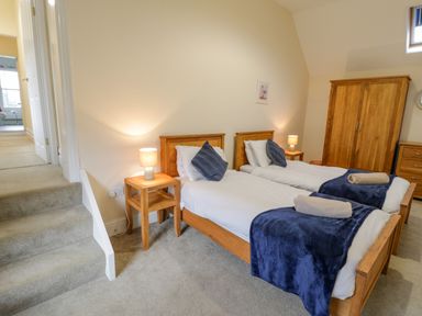 A bedroom with two single beds wooden furniture and blue throws at The Farm House in Bala