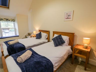 A bedroom with two single wooden beds bedside tables lamps and a window at The Farm House in Bala