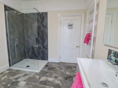 A bathroom with a walk-in shower a white door a white towel rack with a pink towel and a white sink with soap at The Farm House in Bala