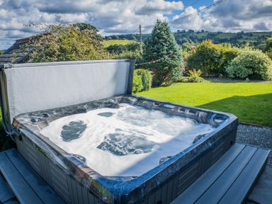 An outdoor hot tub with bubbling water in a garden with trees and hills in the background at The Farm House in Bala