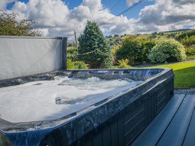 An outdoor hot tub with bubbles and a partially open cover in a garden with trees and bushes at The Farm House in Bala