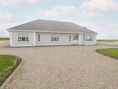 A single story house with multiple windows and a large gravel driveway at Shraigh Beach in Belmullet County Mayo