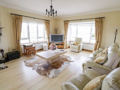 A living room with cream sofas a coffee table a TV and large windows at Shraigh Beach in Belmullet County Mayo