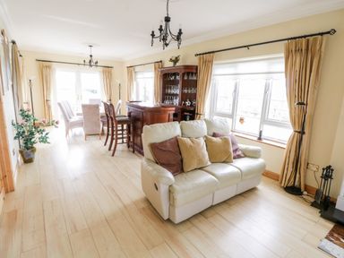 A living room with a cream leather sofa and pillows a wooden bar dining table with chairs and beige curtains at Shraigh Beach in Belmullet County Mayo