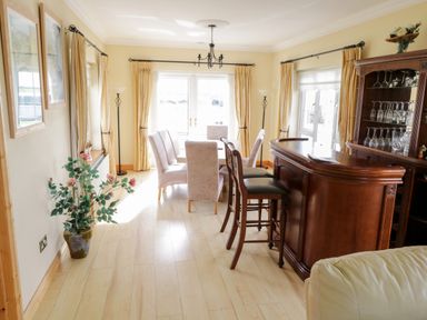 A dining room with a wooden bar, dining table and chairs with large windows and curtains at Shraigh Beach in Belmullet County Mayo