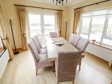 A dining room with six chairs around a table and windows showing outdoor greenery at Shraigh Beach in Belmullet County Mayo