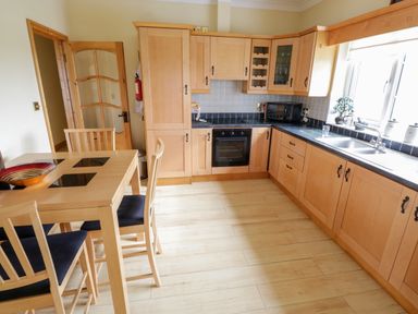 A kitchen with wooden cabinets a black oven a dining table with chairs and a window at Shraigh Beach in Belmullet County Mayo