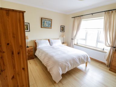 A bedroom with a double bed with white bedding wooden wardrobes bedside tables lamps and a window with curtains at Shraigh Beach in Belmullet County Mayo