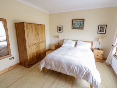 A bedroom with a double bed between two wooden nightstands each with a lamp a wooden wardrobe and a large mirror on the wall at Shraigh Beach in Belmullet County Mayo