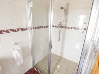 A bathroom shower area with glass doors a showerhead a towel ring with a towel and beige tiles at Shraigh Beach in Belmullet County Mayo