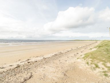 A sandy beach with scattered pebbles and grass dunes near the shore at Shraigh Beach in Belmullet County Mayo