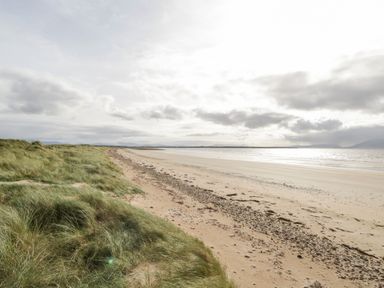 A sandy beach with grass covered dunes beside it under a cloudy sky at Shraigh Beach in Belmullet County Mayo