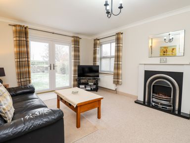 A living room with a black leather sofa and wooden coffee table near a fireplace and TV at Darling Cottage in Bamburgh