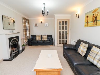 A living room with two black leather sofas a wooden coffee table a fireplace and wall art at Darling Cottage in Bamburgh