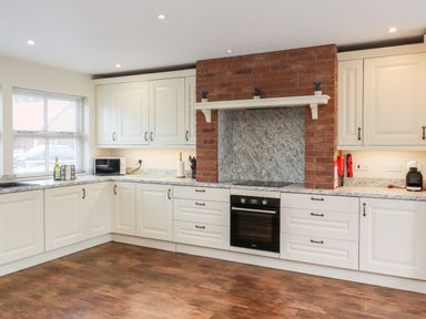 A kitchen with white cabinets a brick oven area and wooden floor at Darling Cottage in Bamburgh
