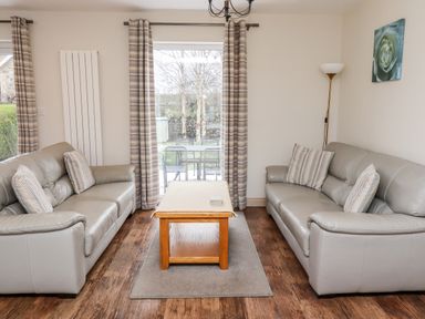 A living room with two sofas facing each other a wooden coffee table and patterned curtains at Darling Cottage in Bamburgh