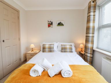 A bedroom with a double bed two bedside tables with lamps plaid cushions and a window with plaid curtains at Darling Cottage in Bamburgh