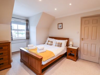 A bedroom with a wooden bed with white bedding and yellow throw at Darling Cottage in Bamburgh