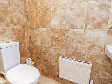 A bathroom with a white toilet a roll of toilet paper on a small ledge a radiator and a small portion of a white sink Darling Cottage Bamburgh