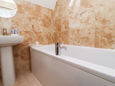 A bathroom with a white bathtub and sink with soap dispensers and a round mirror on the wall at Darling Cottage in Bamburgh