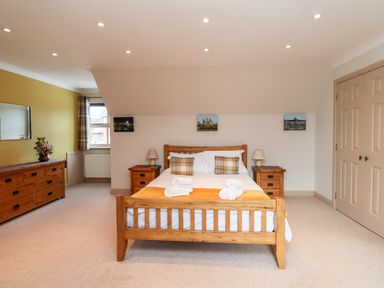 A bedroom with a wooden bed and bedside tables a dresser with flowers and a window at Darling Cottage in Bamburgh