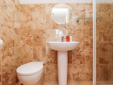 A bathroom with a toilet sink round mirror and glass shelf at Darling Cottage in Bamburgh