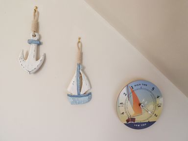 A wall with a wooden anchor, a wooden sailboat, and a tide clock at Darling Cottage in Bamburgh