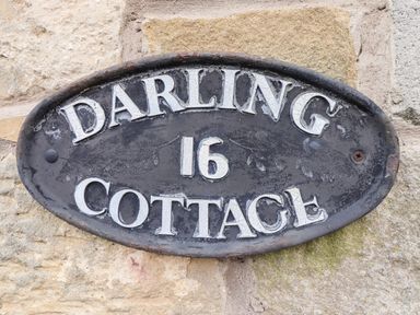 A metal oval sign with the text Darling 16 Cottage on a stone wall at Darling Cottage in Bamburgh