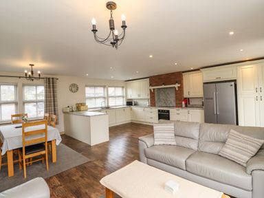 An open-plan kitchen and dining area with wooden chairs around a table a grey sofa and a stainless steel refrigerator at Darling Cottage in Bamburgh