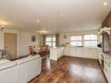 An open plan kitchen and dining area with wooden dining chairs and table at Darling Cottage in Bamburgh