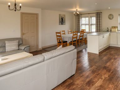 An open living and dining area with sofas, a dining table with chairs, and a kitchen counter at Darling Cottage in Bamburgh