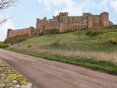 A large stone castle on a hill with a road in the foreground at Darling Cottage in Bamburgh