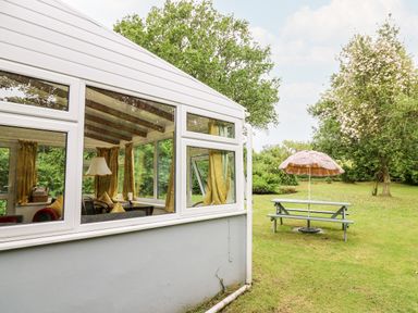 A conservatory with yellow curtains and a lamp next to a garden with a picnic table and a parasol at Maesgwyn in Bridell near Cardigan