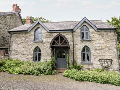 A stone cottage with arched windows and a blue wooden door surrounded by plants at Maesgwyn in Bridell near Cardigan