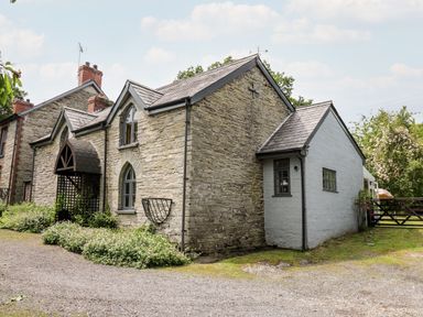 A stone house with arched windows and a wooden porch surrounded by plants at Maesgwyn Bridell near Cardigan
