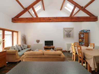 A living room with a sofa and dining area at Riverside Barn in Gilwern near Crickhowell and Abergavenny