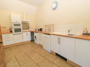 A kitchen with white cabinets wooden countertops a washing machine dishwasher sink and utensils at Keepers Cottage in Winterborne Stickland
