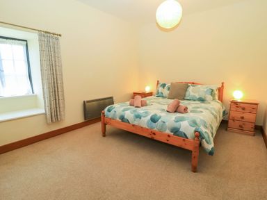 A bedroom with a wooden bed with patterned bedding and two bedside tables with lamps at Keepers Cottage in Winterborne Stickland
